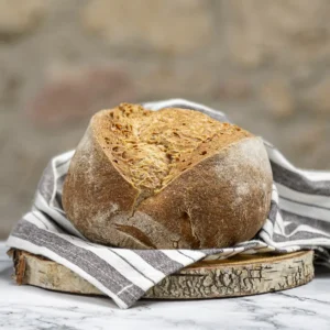 Pan redondo de trigo sarraceno sin gluten con corteza dorada y crujiente, sobre tabla de madera rústica y paño de cocina