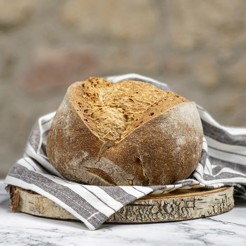 Pan redondo de trigo sarraceno sin gluten con corteza dorada y crujiente, sobre tabla de madera rústica y paño de cocina