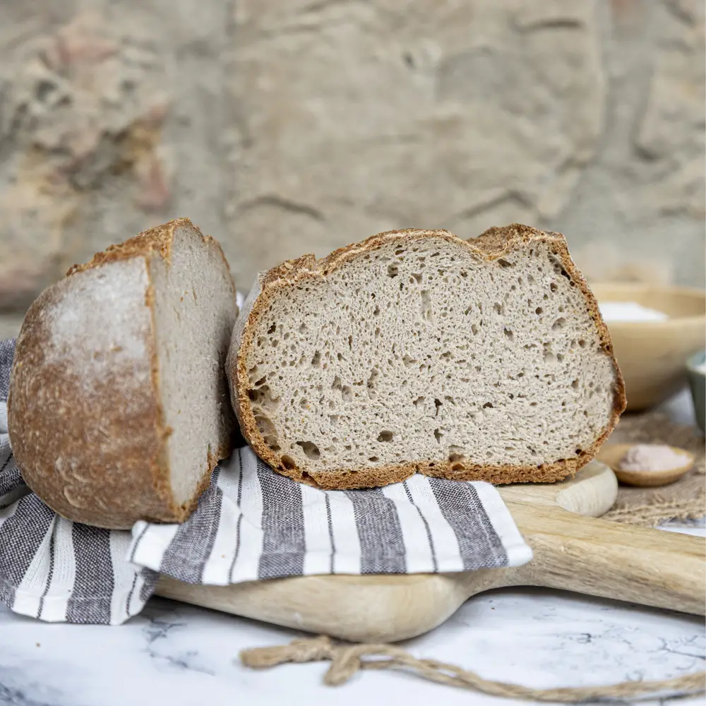 Pan de trigo sarraceno sin gluten artesanal, abierto por la mitad, con miga esponjosa y corteza crujiente sobre tabla de madera