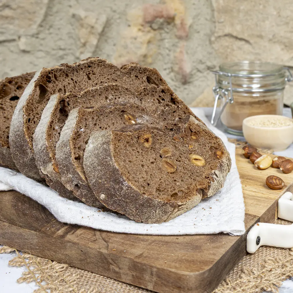 Rebanadas de pan de algarroba sin gluten con avellanas, colocadas sobre una tabla de madera, fondo rústico con ingredientes