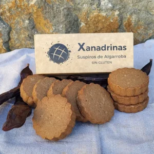 Xanadrinas Suspiros de Algarroba sin gluten, galletas artesanales sobre tela clara y fondo de piedra, junto a su caja de cartón ecológica