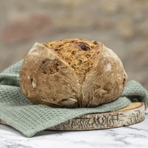 Pan redondo de higos y nueces sobre un paño verde y tabla rústica de madera, con fondo desenfocado de piedra